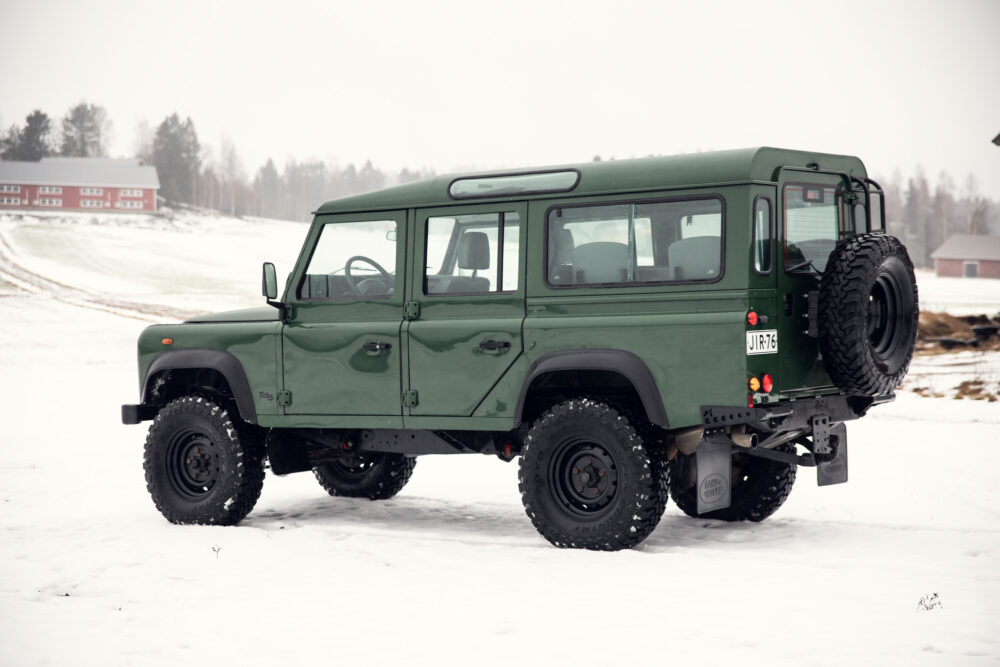 Green SUV on snowy field near red building