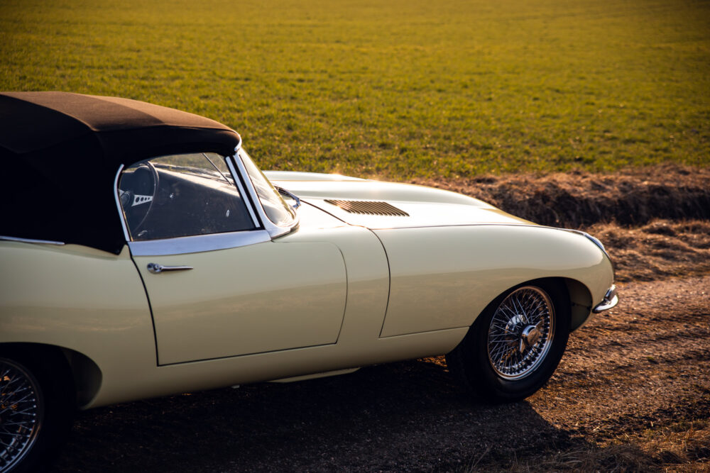 Vintage cream sports car in grassy field at sunset