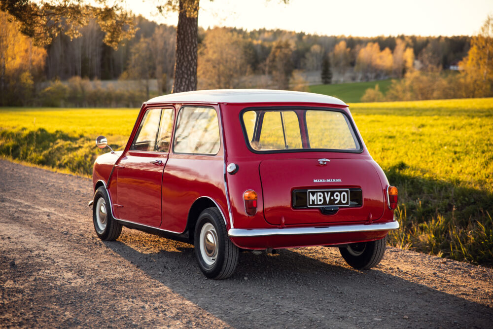 Red vintage Mini Minor car on countryside road at sunset