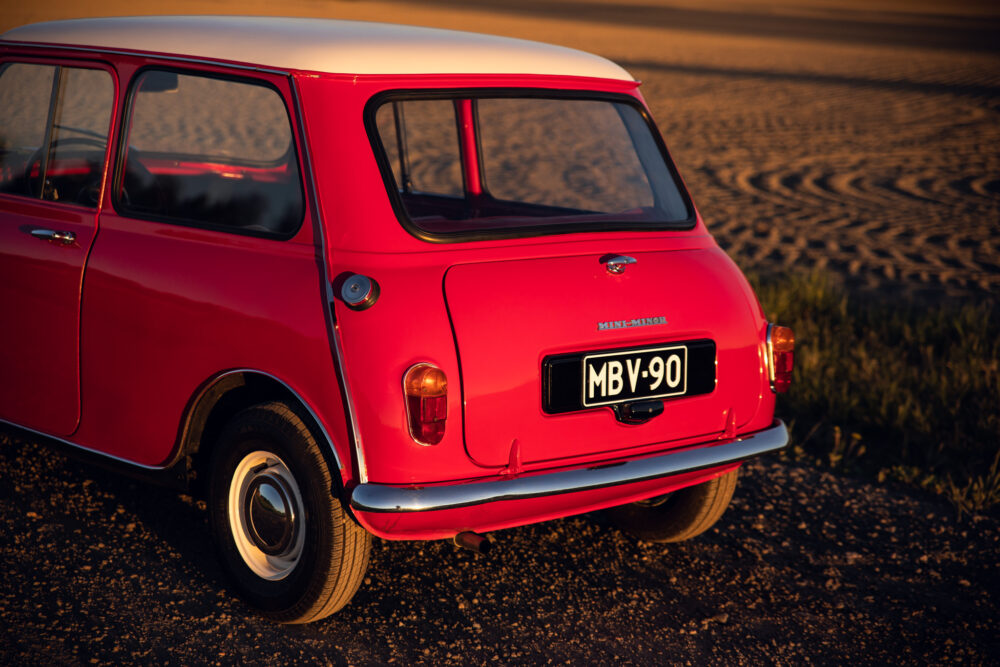 Vintage red Mini Minor car on sandy road at sunset