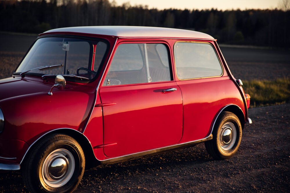 Vintage red Mini Cooper parked in rural setting.