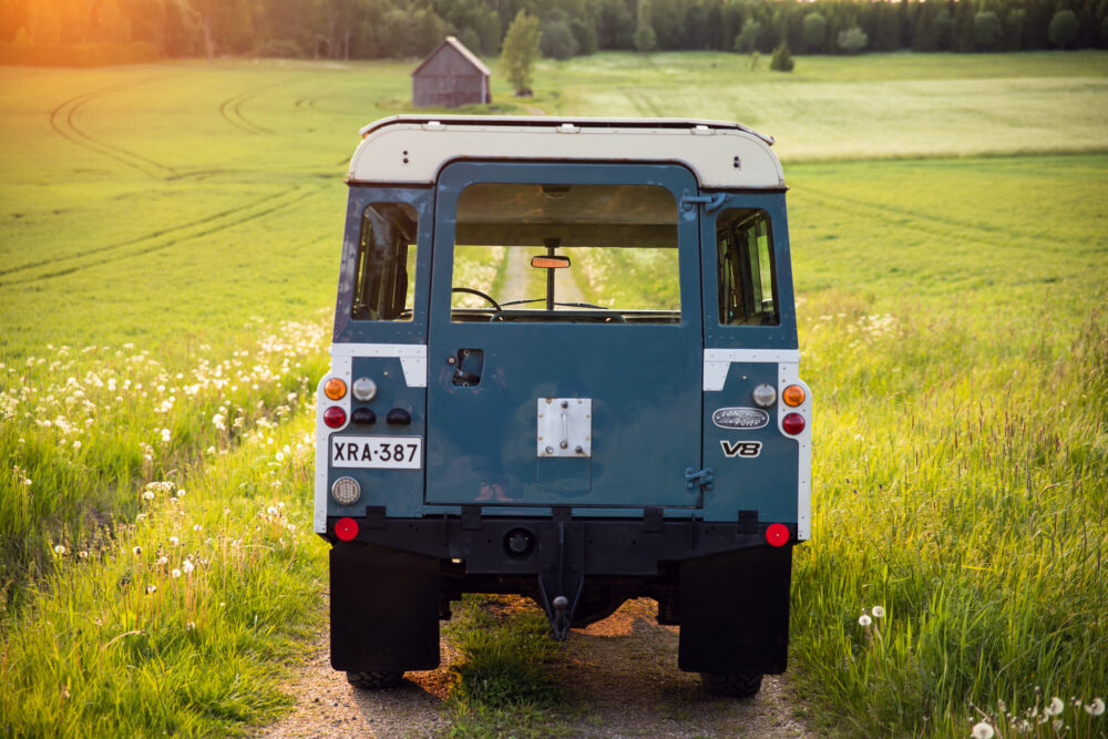 Blue SUV parked on rural path near green field at sunset
