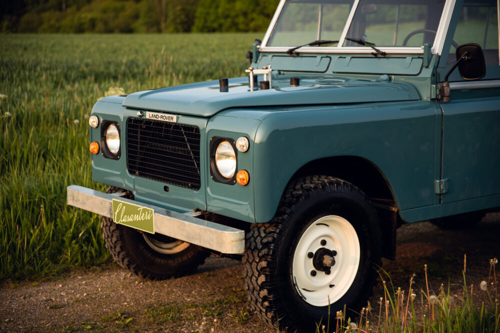 Vintage teal Land Rover parked in green field