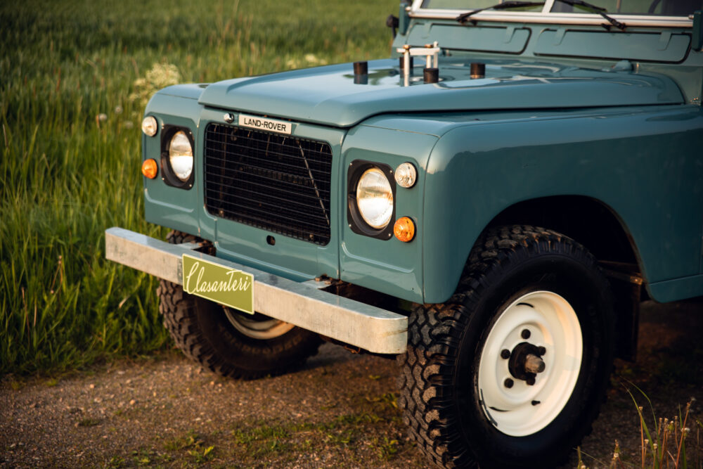 Vintage teal Land Rover in grassy field