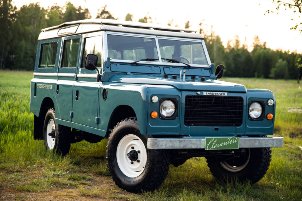 Vintage blue Land Rover in grassy field at dusk