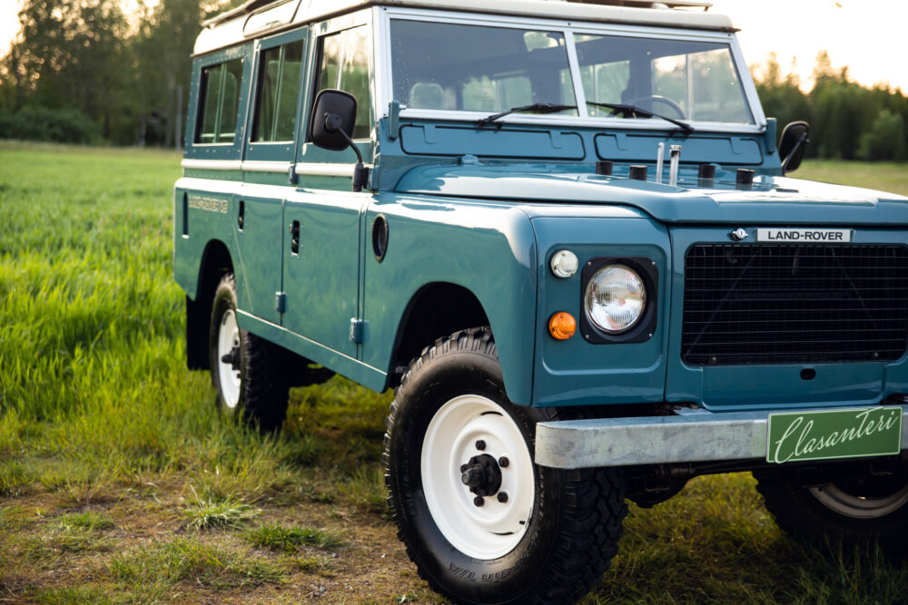 Vintage blue Land Rover in grassy field at dusk