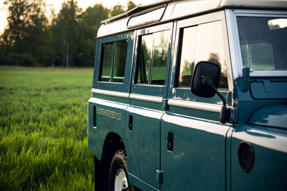 Blue Land Rover V8 parked in grassy field at dusk