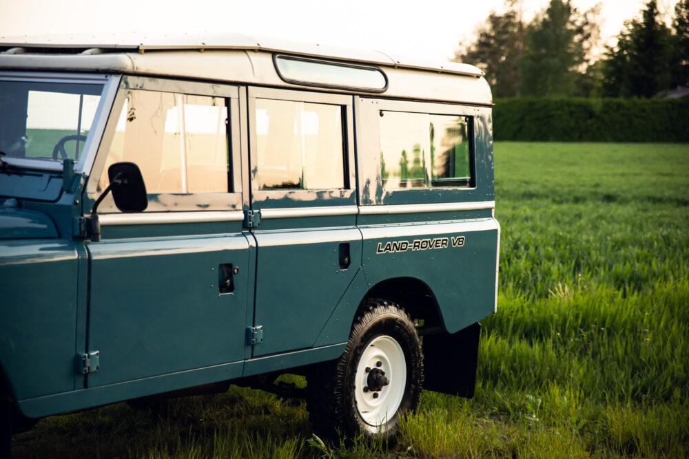 Vintage blue Land Rover V8 parked in green field.
