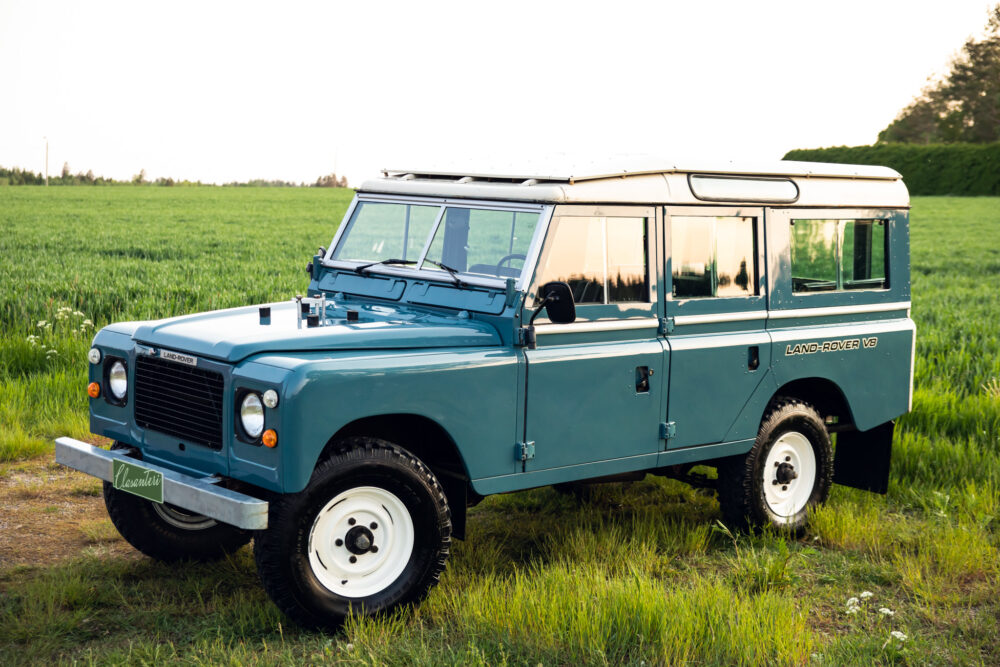 Blue Land Rover V8 on green field at sunset