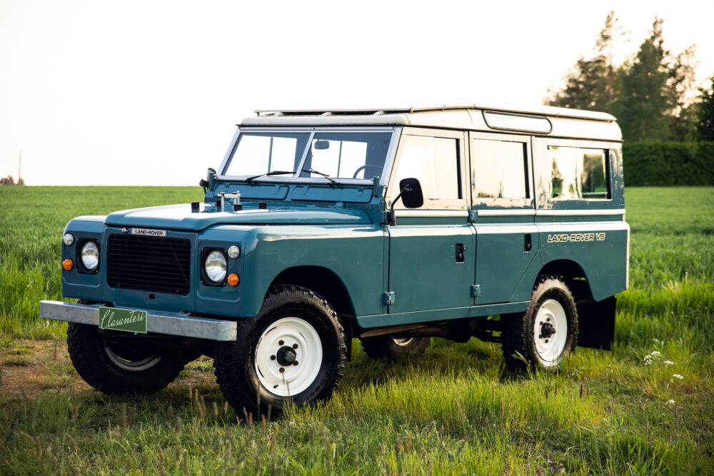 Vintage blue Land Rover in green field at sunset