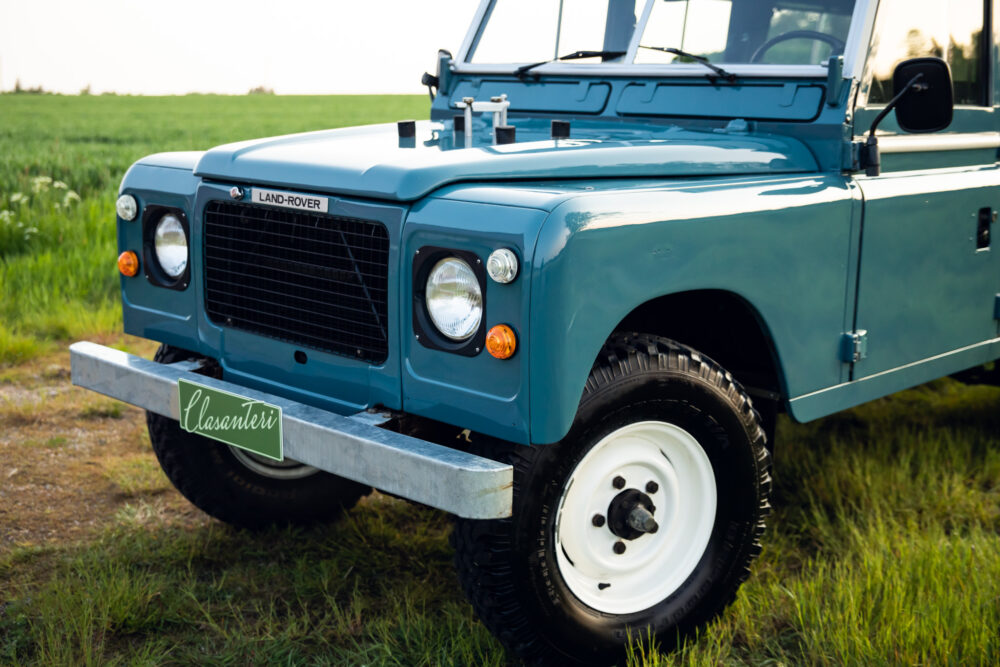 Vintage blue Land Rover parked in grassy field.