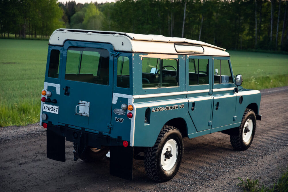 Blue vintage Land Rover V8 parked near a forest