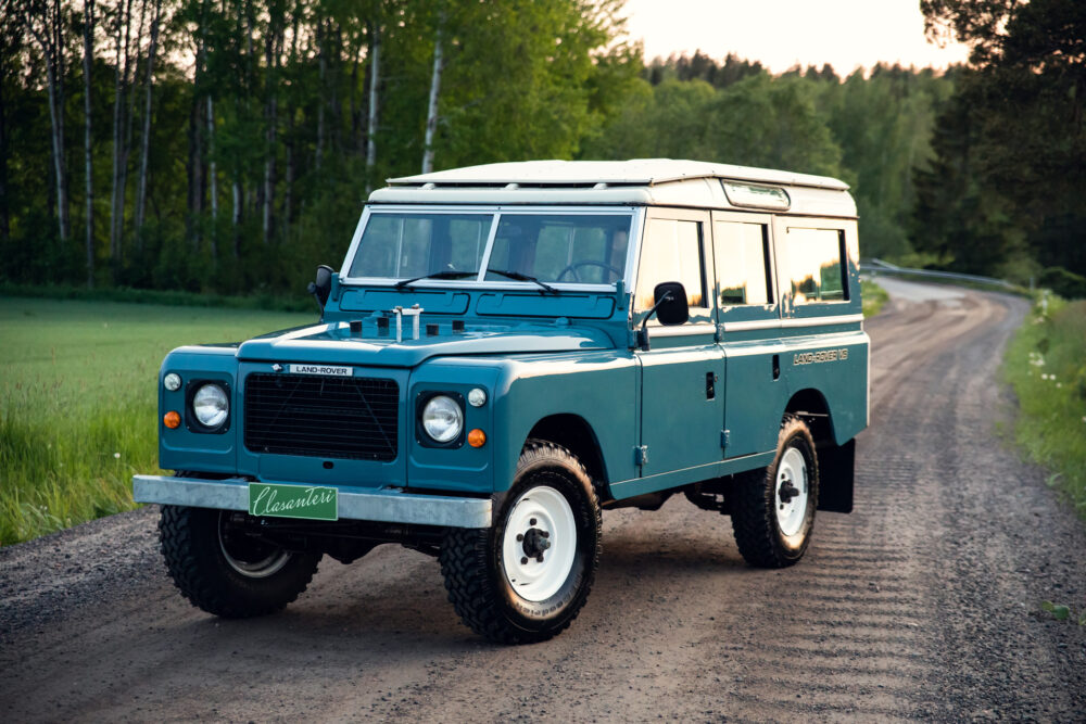 Vintage blue Land Rover on a forest road at dusk