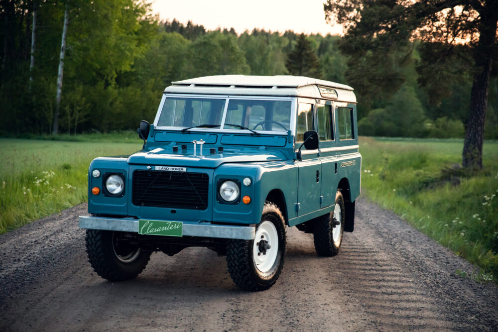 Vintage blue Land Rover on a forest path at dusk