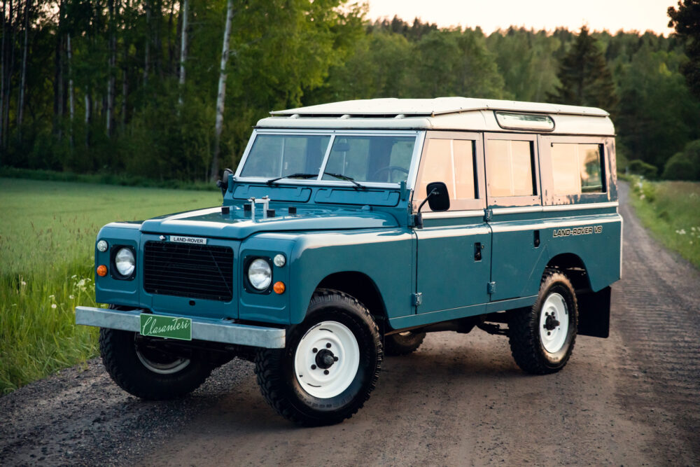 Vintage blue Land Rover on a forest road at dusk