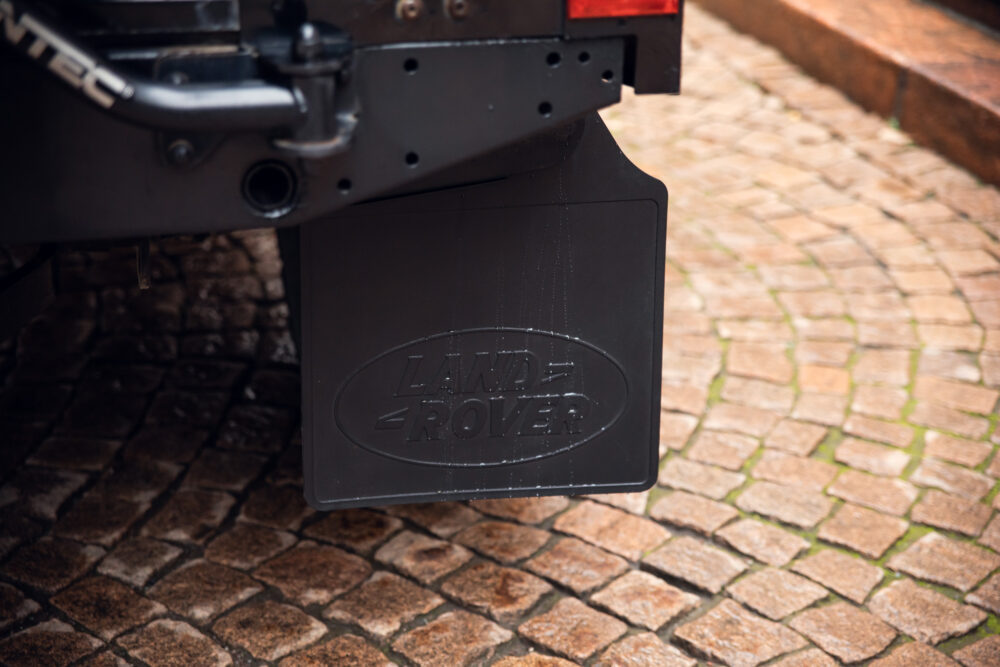 Land Rover logo on black mudflap against cobblestone