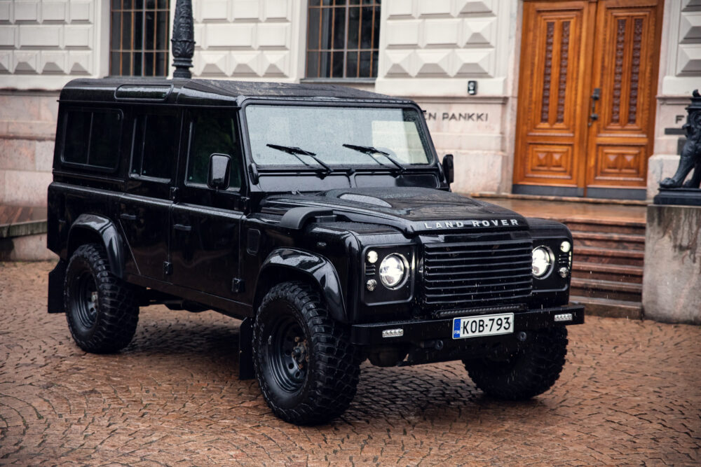 Black Land Rover Defender parked on cobblestone street.