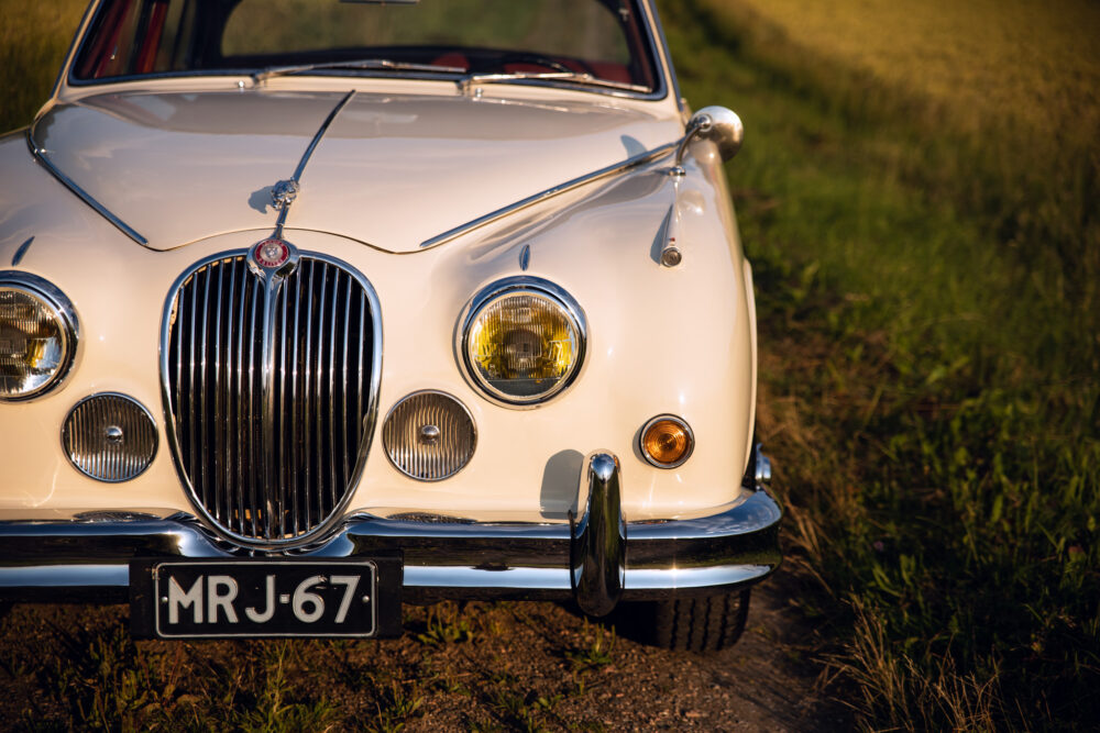 Vintage white Jaguar car parked near field at sunset