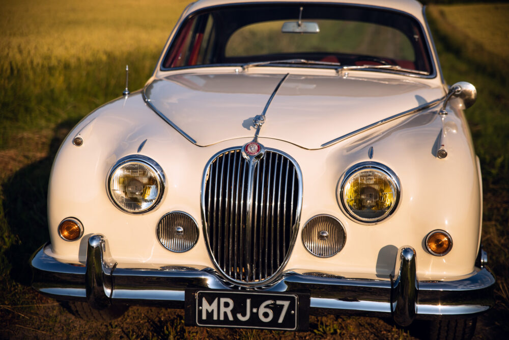 Vintage white Jaguar car in golden field at sunset.