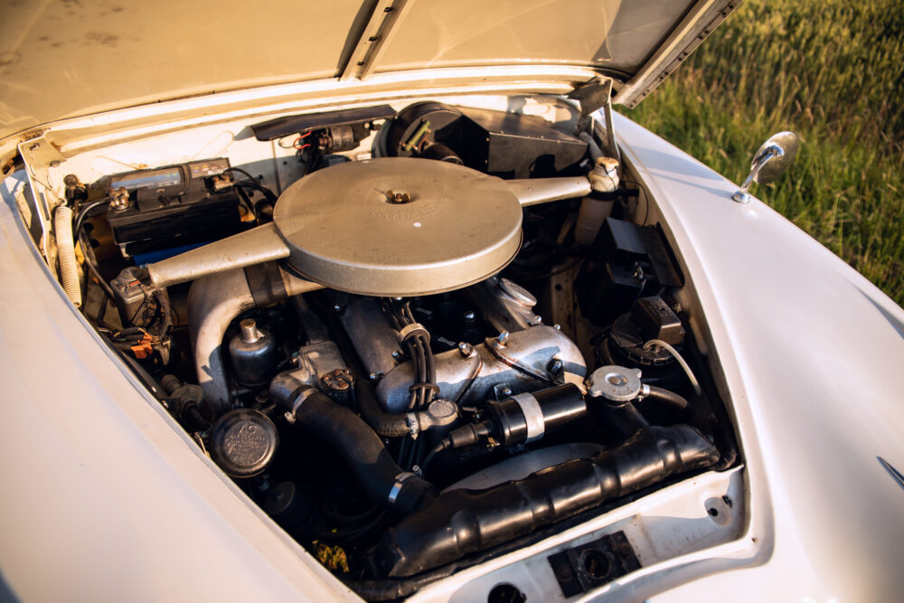 Vintage car engine open in field at sunset