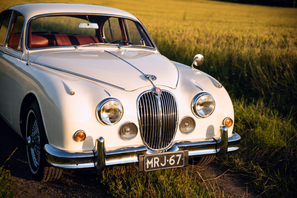 Vintage white Jaguar car in grass field at sunset