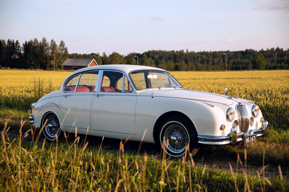 Vintage white Jaguar car in a golden field at sunset