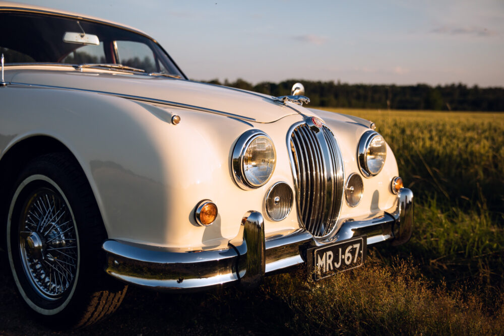 Vintage white Jaguar car in golden field at sunset