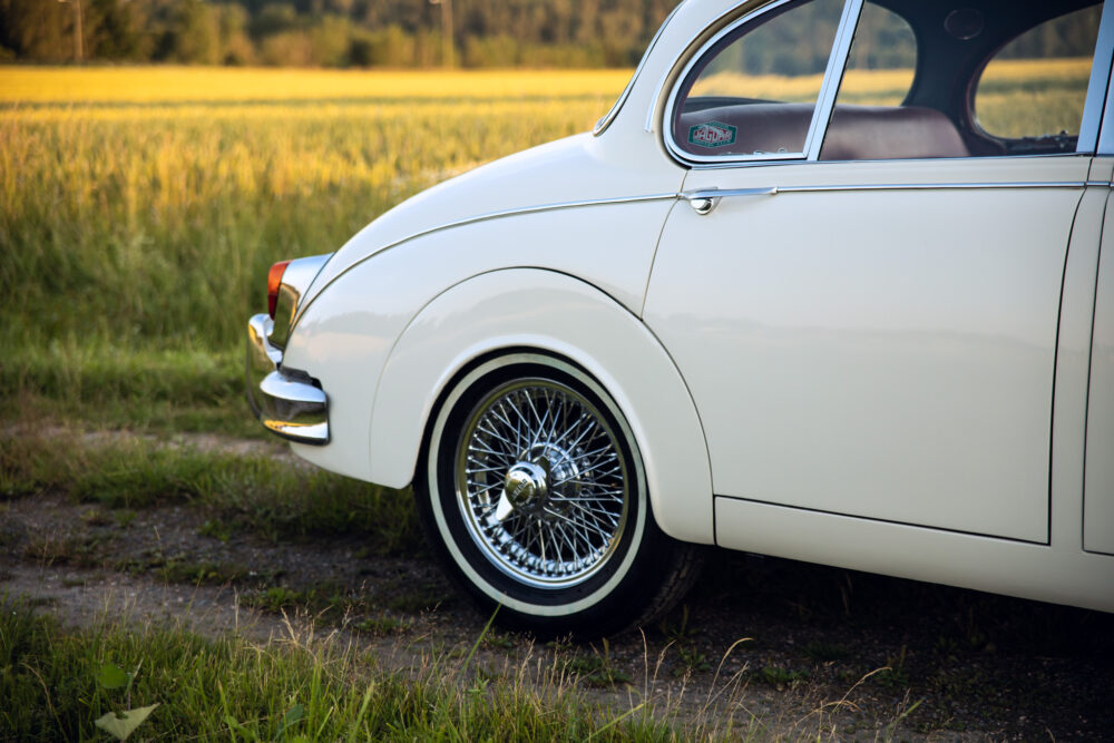 Vintage white car with chrome spokes near a field