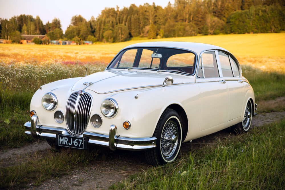 Vintage white Jaguar car in a scenic field at sunset