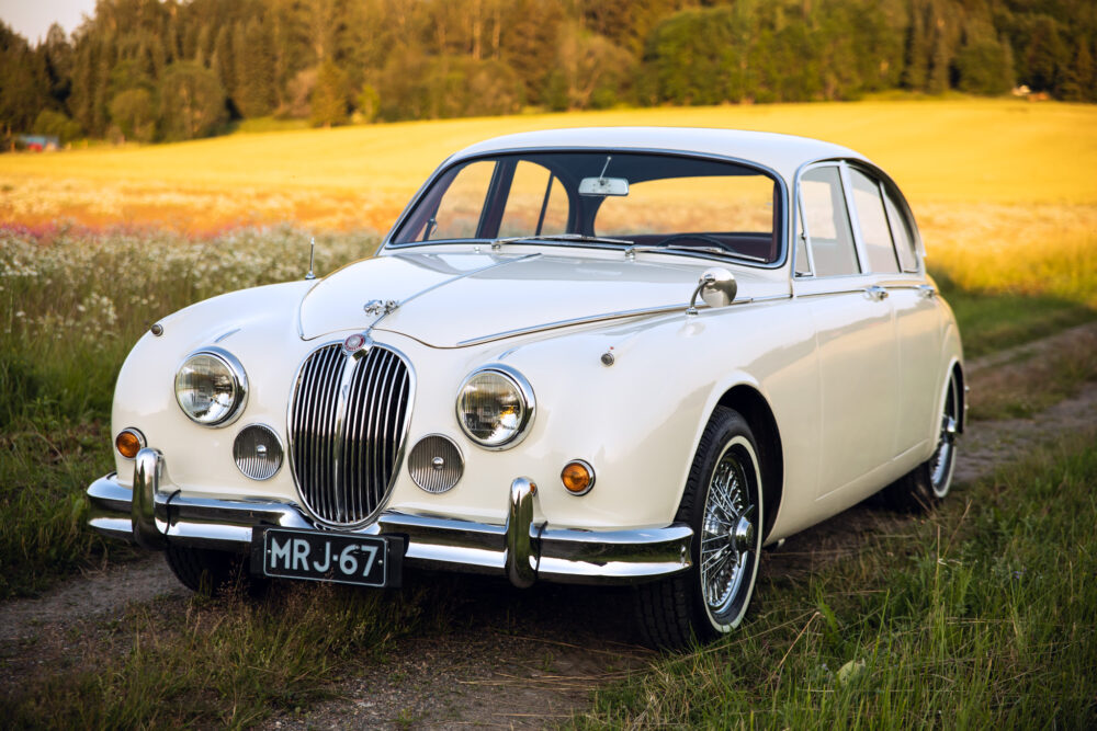 Classic white Jaguar car parked in a colorful meadow