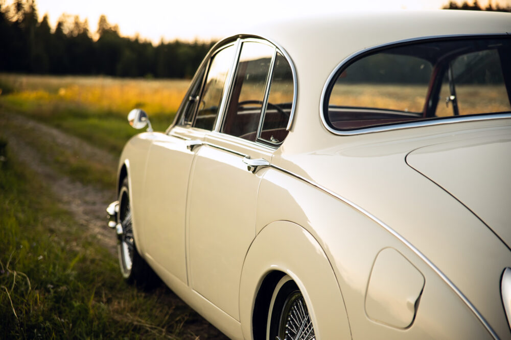 Vintage white car parked beside country road at sunset