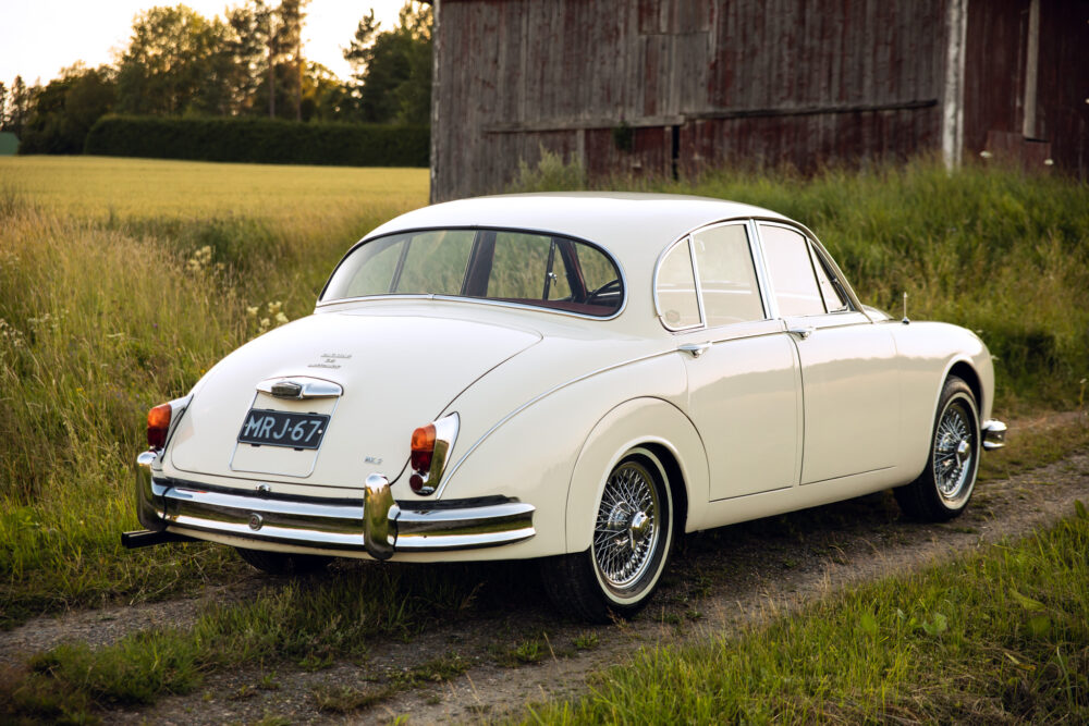 Vintage white Jaguar car parked by barn in field