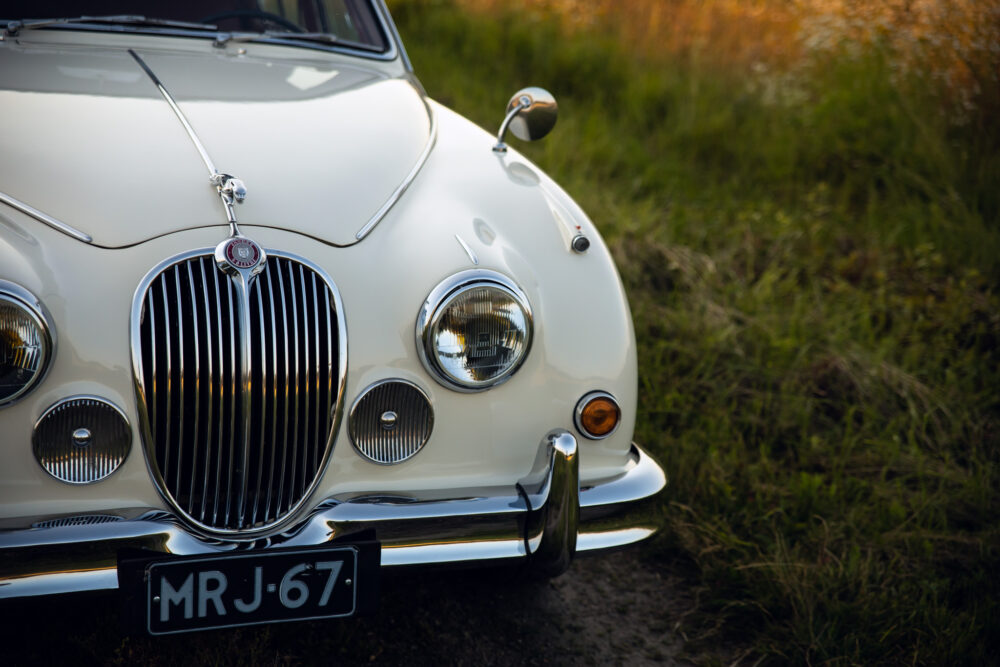 Vintage white Jaguar car on grassy roadside.