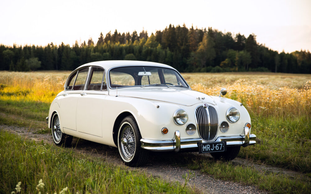 Vintage white Jaguar car in rural field at sunset