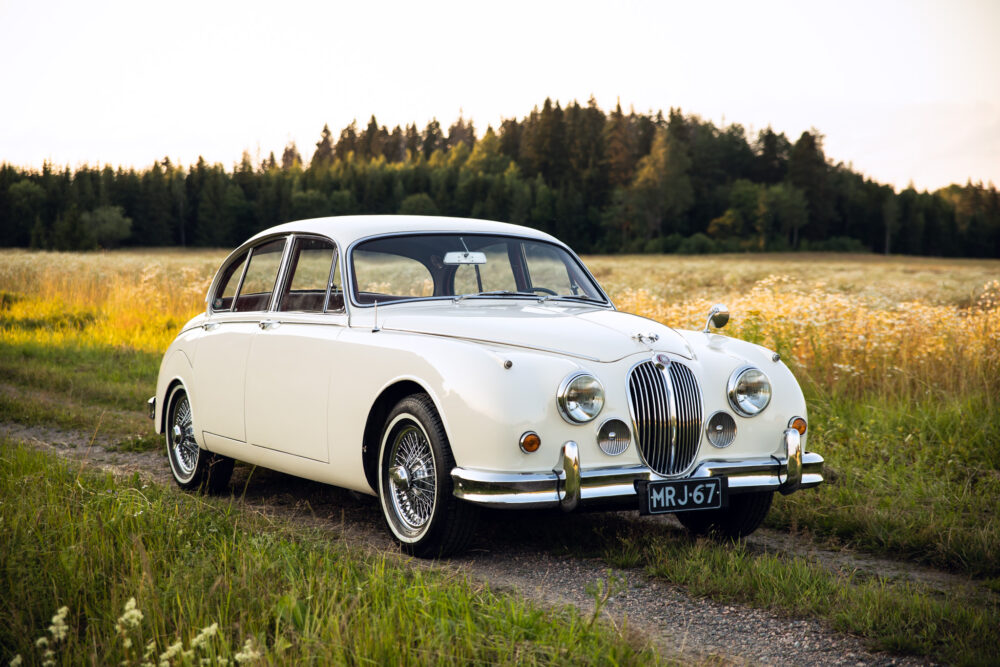 Vintage white Jaguar car in rural field at sunset