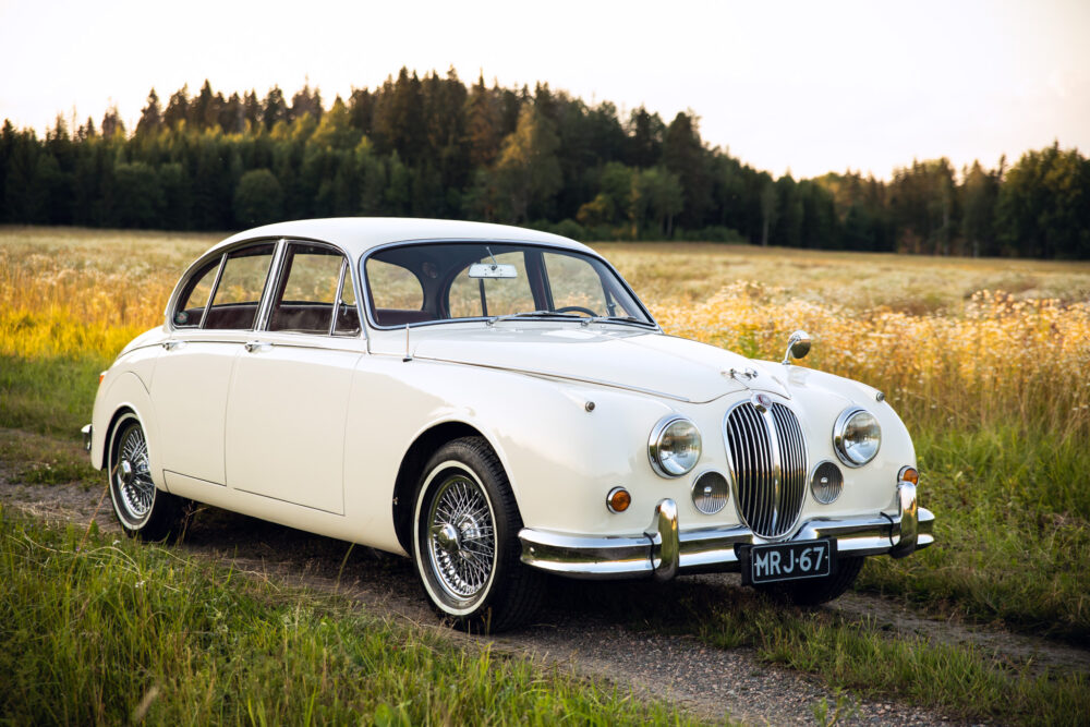 Vintage white Jaguar car in a field at sunset