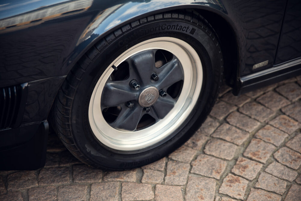 Classic Porsche wheel with Continental tire on cobblestone.
