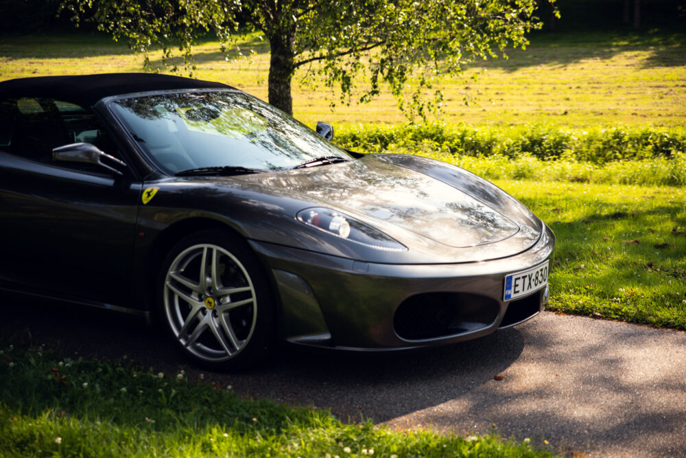 Silver Ferrari parked beside trees on sunny day