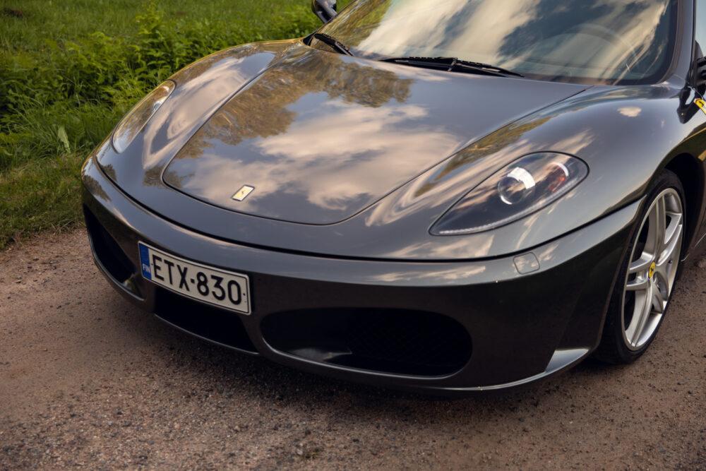 Black Ferrari parked on a dirt road beside grass