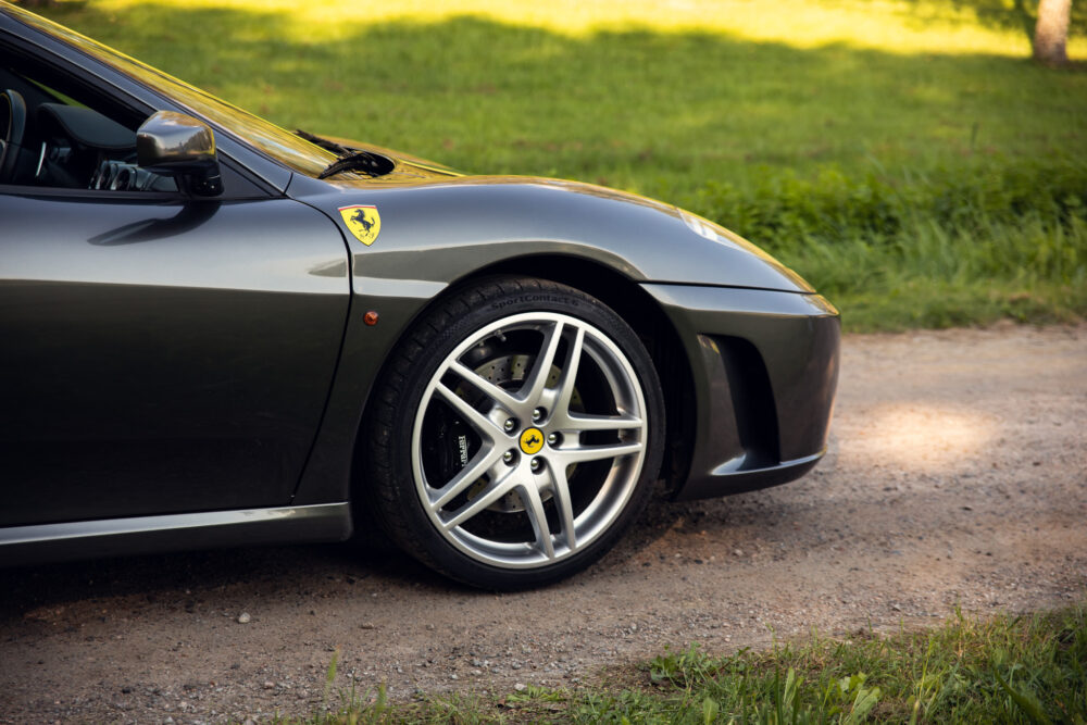 Gray Ferrari parked on a dirt road near trees