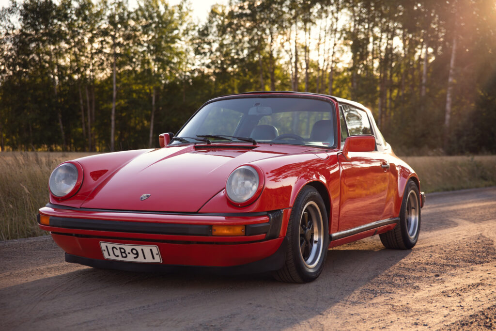 Red vintage Porsche car on forest road at sunset