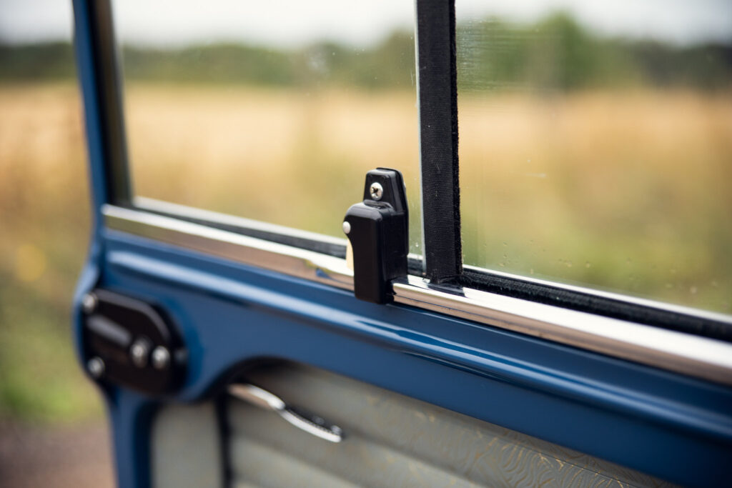 Close-up of a bus window and latch overlooking field
