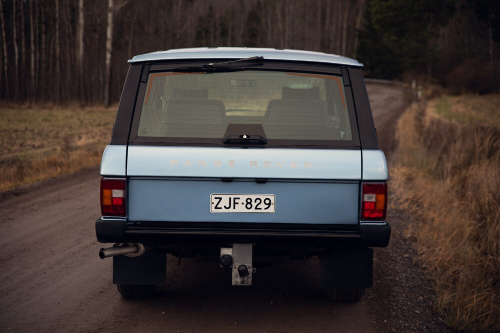 Vintage blue Range Rover on a rural dirt road.