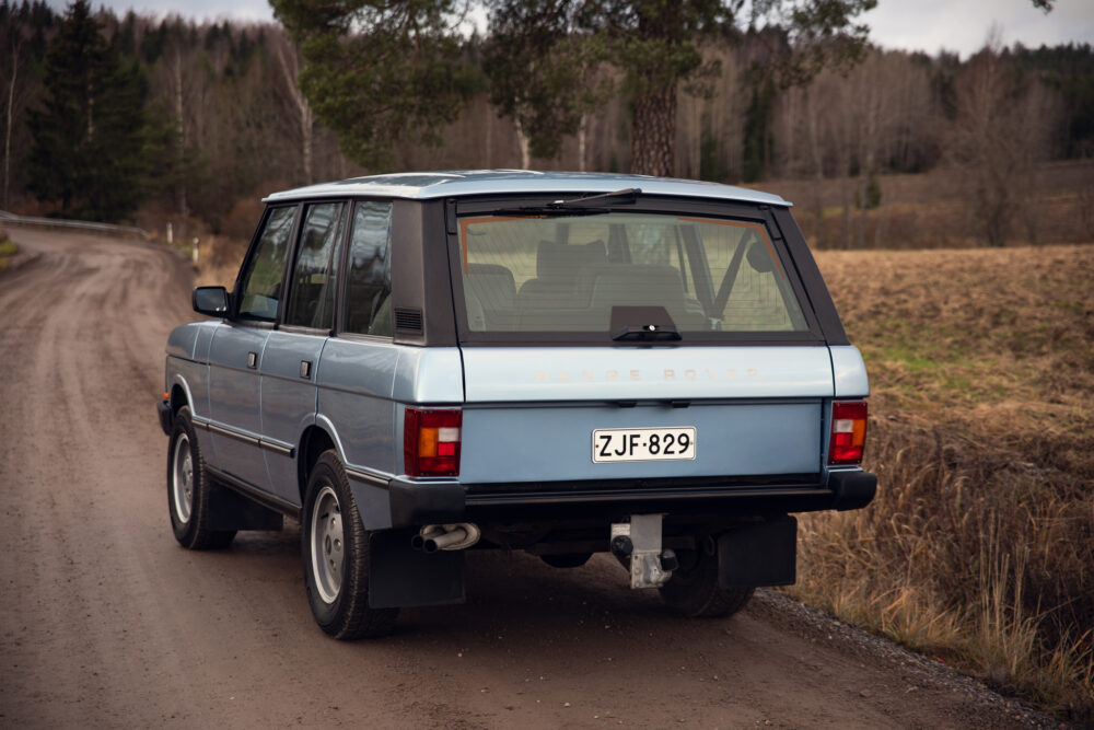 Vintage blue Range Rover on forest dirt road