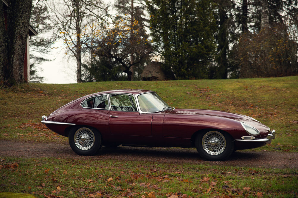 Vintage maroon Jaguar E-Type on grass with trees