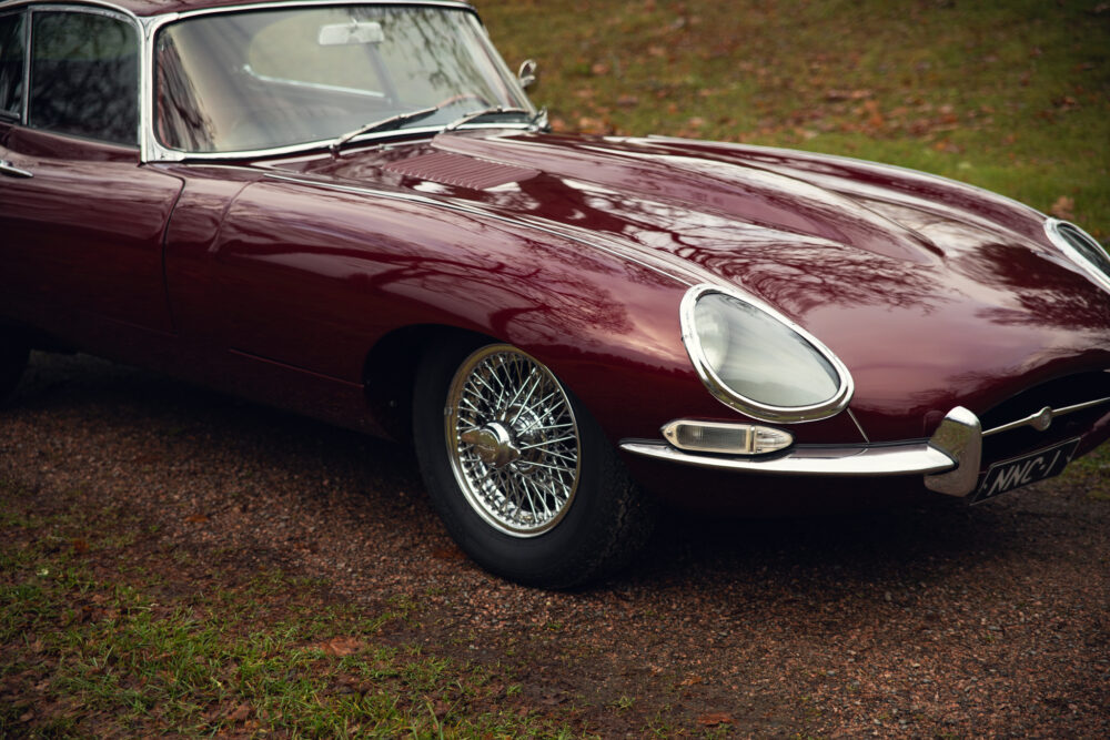 Vintage burgundy Jaguar E-Type on a leafy road