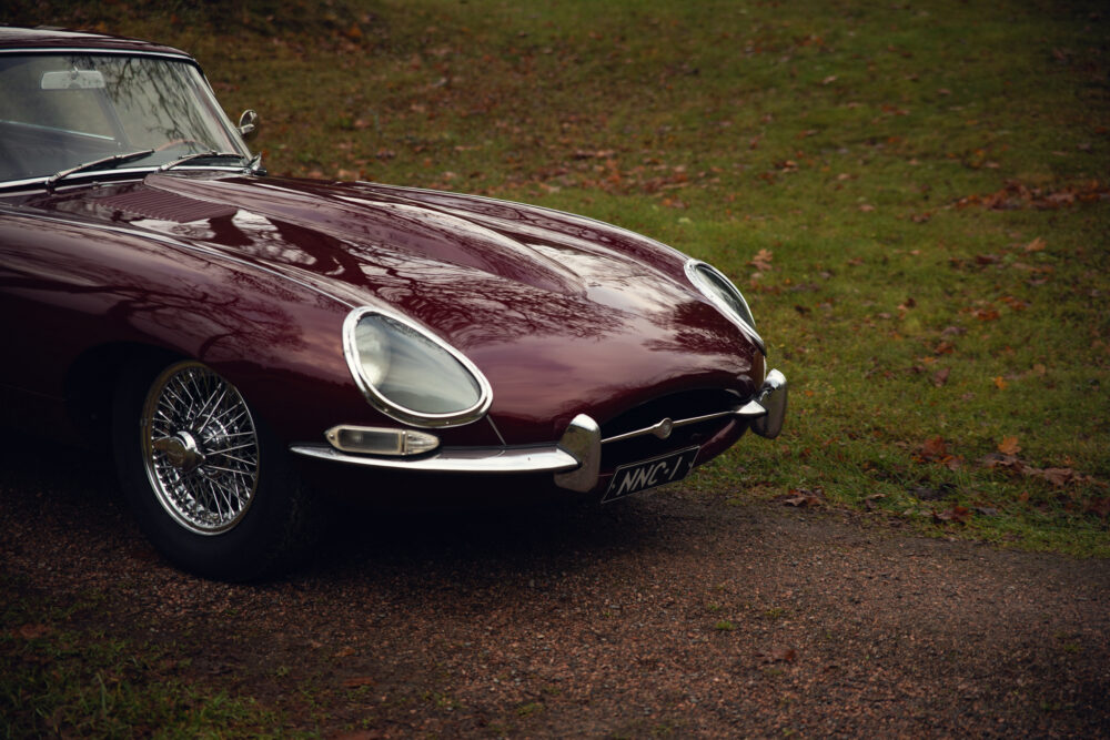 Vintage maroon Jaguar E-Type on autumn leaf-strewn path
