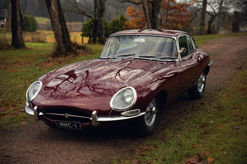 Vintage maroon Jaguar E-Type on a scenic autumn road