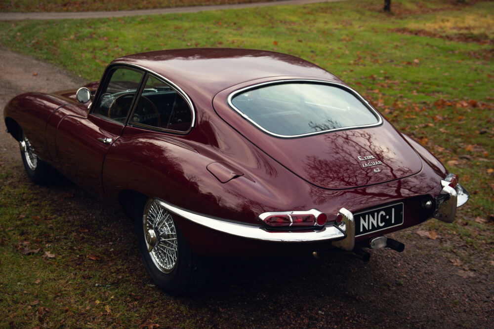 Vintage maroon Jaguar E-Type car on leafy road