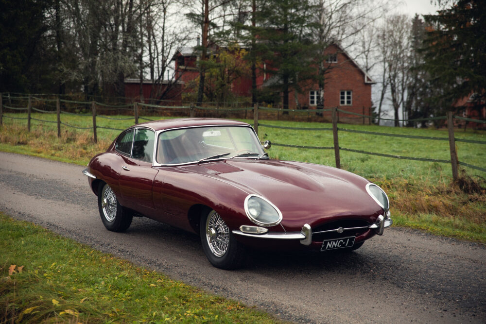 Vintage maroon coupe on rural road near brick house